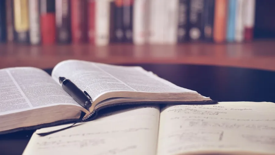 An open textbook and a notebook of handwritten revision notes in front of a bookshelf