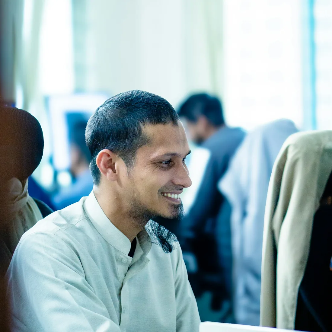 A tutor wearing headphones teaching a live online English lesson, holding up a notebook of worked grammar examples to the camera